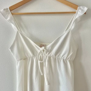 Vit sommartopp från Nelly - Superfint vitt linne från Nelly med smala axelband och v-ringning. Linnet har knyt framtill och är gjord i ett lätt, strukturerat tyg som känns luftigt. Perfekt för varma dagar och har en enkel men söt design.