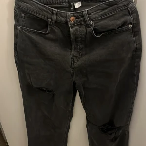 Svarta jeans från Divided med slitningar - Svarta jeans från Divided med snygga slitningar på knäna. Klassisk femficksmodell med knapp och dragkedja. Jeansen har en tvättad look och raka ben. Perfekta för en avslappnad och trendig stil.