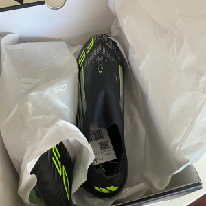 Adidas F50 svarta fotbollsskor - Snygga Adidas F50 fotbollsskor i svart med neonfärgade detaljer och modern design. Skorna har en strömlinjeformad form och är tillverkade i syntetmaterial för bästa prestanda på planen. Perfekta för dig som vill sticka ut på matchen.