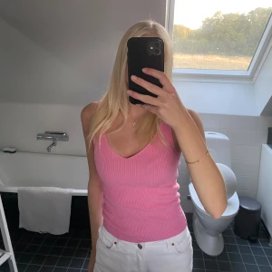 Rosa ribbad linnetopp - Säljer en söt rosa ribbad linnetopp med v-ringning. Toppen är ärmlös och har en tight passform som framhäver figuren. Perfekt för varma dagar och enkel att matcha med jeans eller kjol.