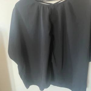Svart blus med snörning bak - Svart blus från EXTENDED2.0 i storlek L. Modellen har en lös passform och korta ärmar. Snygg detalj med snörning i v-ringad form baktill. 30kr+frakt