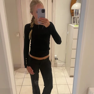 Svart långärmad tröja från Zara - Svart långärmad tröja från Zara med rund hals och slim passform. Tröjan har snygga guldfärgade knappar på ärmsluten som ger en extra detalj. Mjuk och stretchig. Enkel och stilren design som funkar året runt.