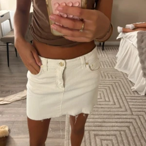 Vit jeanskjol med rå kant - Vit kort jeanskjol med rå, fransig kant nertill och klassiska fickor fram och bak. Kjolen har bälteshällor och stängs med knapp och dragkedja. Perfekt för en chill och trendig look.