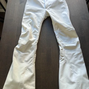 Vita täckbyxor med markerade sömmar - Säljer ett par snygga vita skidbyxor. Byxorna har en clean, stilren look. Materialet är slitstarkt och håller dig varm i backen. 