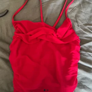 Rött linne med smala axelband - Snygg röd kortklänning med smala axelband och draperad överdel. Perfekt för dig som vill sticka ut med en färgstark look. Klänningen har en figurnära passform och är tillverkad i ett mjukt material som känns skönt mot huden.