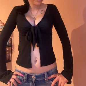 Svart omlottopp med knyt Gina Tricot - Svart långärmad omlottopp från Gina Tricot i storlek XXS. Toppen har djup v-ringning och en snygg knytning framtill som ger en croppad look. Perfekt att styla med jeans eller kjol för en trendig outfit.