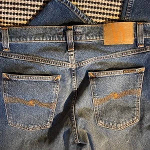 Nudie Jeans Solid Ollie Wild Blue  - Snygga blå jeans från Nudie Jeans i modellen Solid Ollie Wild Blue. Klassisk femficksdesign med orangea sömmar och ikonisk brodyr på bakfickan. Tillverkade i 99% bomull och 1% elastan för en skön passform. Köpta från Åhléns och aldrig använda (har kvar kvitto)