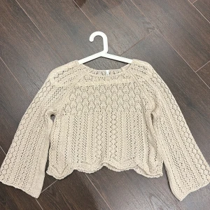 Beige stickad tröja från ONLY - Säljer en beige stickad tröja från ONLY i storlek XS. Tröjan har ett snyggt hålmönster och vågig nederkant, samt långa ärmar. Perfekt för dig som gillar en chill och boho-inspirerad stil. Materialet är mjukt och luftigt, vilket gör den skön att bära under vår och sommar.