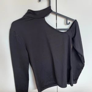 Svart oneshoulder topp från Amisu XS - Säljer en svart långärmad topp från Amisu i storlek XS. Toppen har en cool oneshoulder-design med hög krage på ena sidan och är tillverkad i mjukt stretchigt material. Perfekt för dig som vill sticka ut med en unik och trendig look.