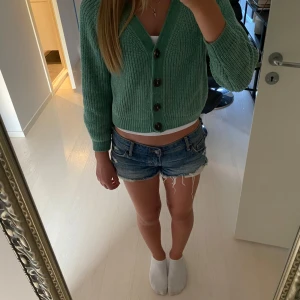 Grön stickad cardigan från H&M - Säljer en grön stickad kofta från H&M med fyra stora knappar framtill. Koftan är croppad och har långärmad design med ribbade muddar och v-ringad hals. Storlek 134/140 men passar super på mig med Xs/S