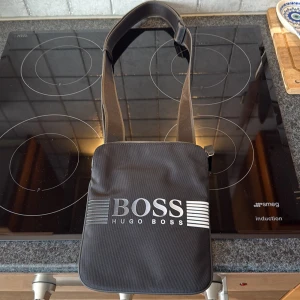 Svart axelväska från Hugo Boss - Säljer min sidoväska från Hugo boss eftersom den inte kommer till användning längre. Väskan är autentiskt och är köpt från zalando. Skriv vid funderingar eller frågor kring fler bilder. Väskan har använts få gånger så ser i princip ny ut.