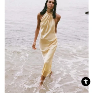 Satin klänning med öppen rygg - Säljer en elegant långklänning i gulfärgat satin med halterneck och knyt i nacken, storlek S. Klänningen har en mjuk, flytande siluett och öppen rygg som ger en riktigt snygg look. Perfekt för sommarkvällar💕