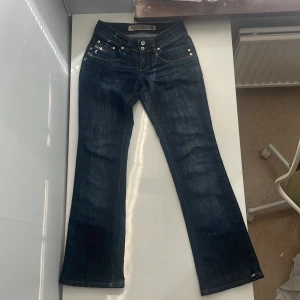 Blå bootcut jeans från Diesel - Snygga blå jeans från Diesel som är  lowrise bootcut passform och klassiska kontrastsömmar. Jeansen har dubbla knappar i midjan, nitar vid fickorna och coola slitningar.