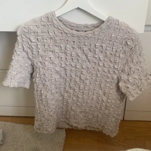 Beige ribbad topp från Lindex - Säljer en beige topp från Lindex i storlek M. Den har ett ribbat, strukturerat tyg med korta ärmar och rund hals. Perfekt för dig som gillar unika detaljer och mjuka material. Passar dig som vill ha en chill och snygg look.