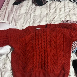 Röd stickad tröja från b.young - Säljer en snygg röd stickad tröja från b.young i storlek XS. Tröjan har ett grovt kabelstickat mönster framtill och på ärmarna, rund hals och långa ärmar. Perfekt för dig som gillar mysiga och trendiga plagg med lite volym.