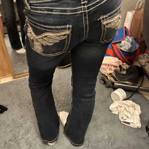 Svarta jeans med broderade fickor Gina Tricot - Säljer ett par svarta jeans från Gina Tricot med kontrasterande vita sömmar och snygga broderade detaljer på bakfickorna. Modellen har låg midja och bootcut-ben, vilket ger en cool och trendig siluett. Perfekt för dig som gillar statement-jeans med unika detaljer. Det finns några fläckar på både benen men det syns inte jättemycket. Det finns bilder på fläckarna☺️