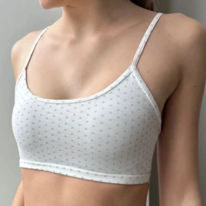 Brandy bralettes - Två söta Bralettes från Brandy Melville, en svart med små vita blommor och en vit med små grå hjärtan. Båda har smala, justerbara axelband och ärmlös design. Perfekta för varma dagar eller som lager under andra plagg. (Man kan köpa en för 50kr)
