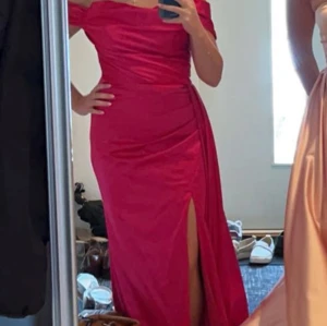 Rosa offshoulder balklänning - Säljer en snygg röd långklänning med offshoulder och slits framtill. Klänningen har en figurnära passform och är perfekt för dig som vill sticka ut. 