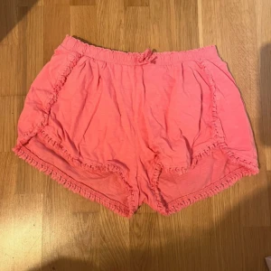 Rosa volangshorts från Zara Girls - Supersöta rosa shorts från Zara Girls med volangdetaljer längs kanterna och mjuk resår i midjan. De är tillverkade i lätt bomull och har en loose passform som är perfekt för varma dagar. Färgen är ljusrosa och shortsen har en feminin vibe.
