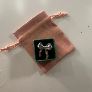 Söt silverfärgad rosettring - Unik ring i form av en stor rosett i blank silverfärg. Ringen har en lekfull och trendig design som verkligen sticker ut. Perfekt accessoar för att ge din outfit en extra touch av personlighet. Levereras i en söt rosa sammetsliknande påse.