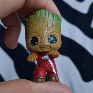 Mini Groot figur - En liten figur av Groot från Guardians of the Galaxy, klädd i röd overall. Det är en söt samlarfigur :)