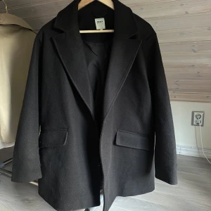 Svart kappa från ONLY i ullmix - Stilren svart kappa från ONLY, i tjockare material. Kappan har haft knappar så man kan stänga den men dom har gått av därav inga knappar, annars är det inga defekter 