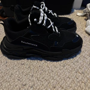 Balenciaga Triple S svarta  - Chunky svarta Balenciaga Triple S sneakers med vit-svarta snören och tydlig logga på sidan, svart-vita snören ingår också. Har använt Max två gånger bara så de är relavivt nya. Skorna va inte riktigt min stil men är perfekta för dig som gillar street-style sneakers. Priset kan diskuteras 