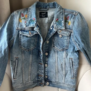 Vintage jeansjacka med broderade blommor - Snygg blå jeansjacka från Denim Co. med broderade blommor i flera färger på. Perfekt för dig som vill ha en unik touch på din outfit. Sparsamt använd och i gott skick. Strl XS/S