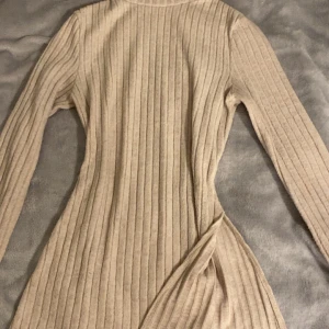 Beige ribbad långärmad tröja  - Säljer en beige ribbad tröja med lång ärm och figurnära passform. Klänningen har en snygg slits vid höften och är tillverkad i ett mjukt stickat material som känns skönt mot huden. Har använt flera gånger och är jätte fint till jeans. 