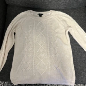 Beige stickad kabeltröja från H&M - Säljer en beige stickad tröja från H&M med klassiskt kabelstickat mönster framtill. Rund halsringning och långa ärmar med ribbade muddar. Perfekt för lager-på-lager och chill stil. 