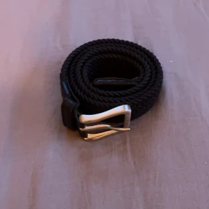 Svart flätat bälte från Jack nand Jones - Snyggt svart bälte med flätad design och silverfärgat metallspänne. Från Jack and Jones. Längd, 95. Bältet har detaljer i skinn vid spännet och är perfekt för att ge en stilren touch till din outfit. Passar både jeans och chinos.