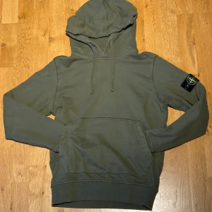 Grön stone island hoodie - Tja, säljer en grön hoodie från Stone Island med klassisk patch på ärmen. Tröjan har huva med snörning, känguruficka och ribbade muddar. Tillverkad i mjuk bomull, perfekt för chill dagar. Stilen är clean och passar dig som gillar en skön stil. Bara skriva om du har frågor! Priset är diskuterbart och skicka gärna ett prisförslag! MVH Brakans Garderob