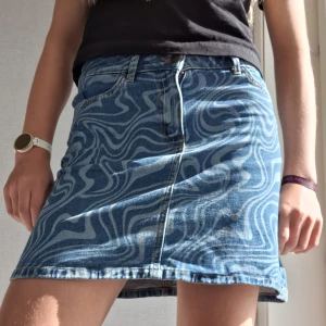 Blå jeanskjol med vågigt mönster Lindex - Säljer en blå jeanskjol från Lindex med coolt vågigt mönster i ljusblått. I storlek 158/164. Kjolen är kort och har klassisk jeansdesign med fickor framtill samt knapp och dragkedja. Perfekt för dig som gillar unika detaljer och denim. Ändast använd ett få tal gånger!