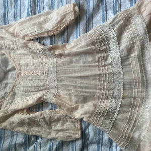  kort klänning med spetsdetaljer - Supersöt ljus kort klänning med spetsdetaljer och knappar framtill. Klänningen har trekvartsärmar, markerad midja med knytband i ryggen och volangkant nertill. Verkligen sååå söt, köpt i Köpenhamn💕