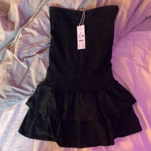 Svart klänning Gina Tricot - Supersnygg svart klänning från Gina Tricot. Klänningen är kort med volangdetaljer nedtill och har en tight passform som framhäver figuren. Materialet är mjukt och stretchigt. Helt oanvänd med prislappen kvar💗