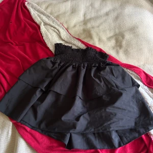 Svart volangkjol från Romwe - Supersöt svart kortkjol från Romwe i storlek M. Kjolen har bred smock i midjan och två lager volanger som ger en riktigt snygg och lekfull look. Perfekt att matcha med en croppad topp eller hoodie för en chill vibe.