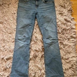 Blå bootcut jeans - Säljer ett par klassiska blå jeans med bootcut passform. Jeansen har fem fickor, normal midja och är tillverkade i ett mjukt denimtyg som ger en skön känsla. Perfekta för dig som gillar en tidlös stil med lite extra vidd vid benslutet.