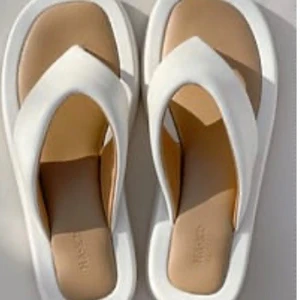 Vita chunky sandaler från NA-KD - Snygga stiliga, bekväma vita sandaler från NA-KD med chunky sula och breda remmar i syntetmaterial. De har en modern, fyrkantig form och mjuk innersula i beige. Perfekta för en trendig sommarlook och superbekväma att glida runt i sandaler. De här flip-flopsen är gjorda av PU och har breda remmar. Man kan gå i dem på långa promenader , på stranden eller promenad i stan. De har rundade tår och vadderade.  Klackhöjd: 3 cm / 1.18 in. De här flip-flopsen kommer i naturvitt. Upper: 100% Polyuretan 