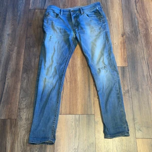 Blå Diesel Belther jeans slim fit - Snygga blå jeans från Diesel, modell Belther, med slitningar och lätt tvättad look. Jeansen har klassisk femficksdesign, smal passform och normal midja. Perfekta för dig som gillar en avslappnad men ändå stilren vibe.