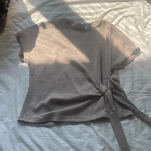 Beige stickad topp med knyt från Zara💞 - Snygg beige stickad topp från Zara med korta ärmar och rund hals. Toppen har en cool knyt-detalj i sidan som ger extra stilpoäng. Materialet är mjukt och har en lätt struktur, perfekt för dig som gillar enkel men trendig design.
