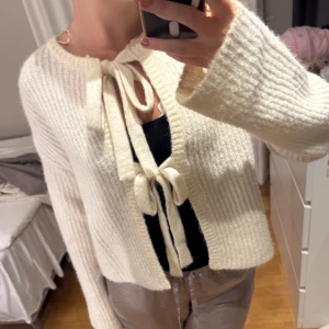 Vit stickad kofta med knytband - Superfin vit stickad kofta med två breda knytband framtill och baktill. Koftan har en loose passform, lång ärm och är ribbstickad för extra mysig känsla. Perfekt att slänga över ett linne för en chill och trendig look.