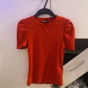 Röd ribbad topp från FB Sister - Superfin röd topp från FB Sister i ribbad bomull med puffiga korta ärmar och rund hals. Sitter snyggt och har en tight passform som framhäver siluetten. Perfekt för dig som gillar färg och vill sticka ut lite extra!