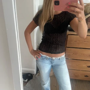 Svart spetstopp med kort ärm - Säljer en svart, tight och genombruten topp med korta ärmar. Toppen är stickad i ett mönster som gör den transparent och passar perfekt över ett linne eller bh. Snygg och trendig att styla till jeans eller kjol. Pris kan diskuteras!