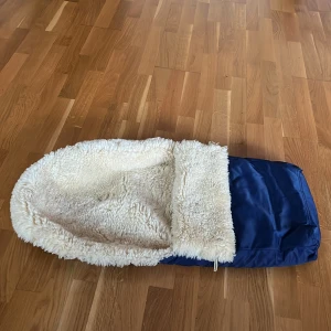 Barnvagn säck med fuskpälsfoder - Mysig barnvagn säck i mörkblått med fluffigt vitt fuskpälsfoder. Utsidan är i slittåligt syntetmaterial och  har en praktisk stor ficka med dragkedja längs sidan. Perfekt för kalla vinterdagar när barnet vill hålla värmen. Ni kan lätt sätta den på erat vagn. Kan diskutera om priset :)