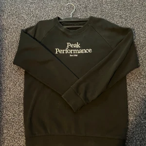 Svart Peak Performance sweatshirt - Svart sweatshirt från Peak Performance med vit broderad logga på bröstet. Klassisk rund hals och ribbade muddar vid ärmslut och nederkant. Mjuk insida i bomullsmix, perfekt för chill eller träning. Snygg och enkel design som funkar till allt. Storleken är S.
