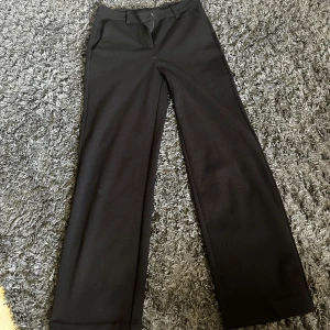 Svarta kostymbyxor från Vero Moda - Stilrena svarta kostymbyxor från Vero Moda med raka, vida ben och klassisk passform. Byxorna har hällor för bälte och stängs med dragkedja och knapp. Perfekta för en clean och snygg look.