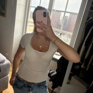 Vit tight t-shirt med djup ringning - Säljer en vit, tight t-shirt med korta ärmar och djup, rundad urringning. Toppen är enkel och stilren, perfekt att matcha med jeans eller kjol. Materialet känns mjukt och följsamt mot kroppen.