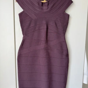 Lila bandageklänning med dragkedja - Snygg lila bandageklänning med tight passform och coola strukturerade paneler. Klänningen är ärmlös och har en markerad axel, samt en synlig dragkedja baktill. Perfekt för dig som gillar en stilren och modern look.