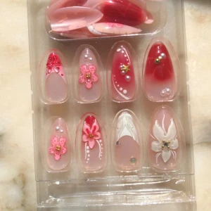 3 set press-on naglar med blommor - Tre olika set med press-on naglar i rosa, nude och rött med 3D-blommor, pärlor och guldiga detaljer. Naglarna har både spetsig och rundad form, vissa med fransk tipp och andra med mönster. Perfekt för dig som vill ha snygga och unika naglar snabbt.