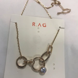 Guldhalsband med cirkelberlocker  - Elegant guldhalsband från RAG med flera cirkelberlocker och en glittrande sten. Kedjan är tunn och smidig, perfekt för att ge en stilren touch till din outfit. Helt ny 